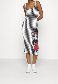 Robe midi sans manches à rayures blanches et noires avec une impression graphique d'un personnage portant des lunettes rouges et un cercle rouge sur la jupe.