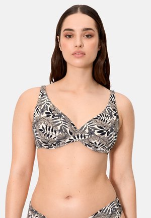 Mujer con el cabello largo y oscuro, con un top de bikini negro y blanco con un patrón de hojas, sobre un fondo claro y liso.