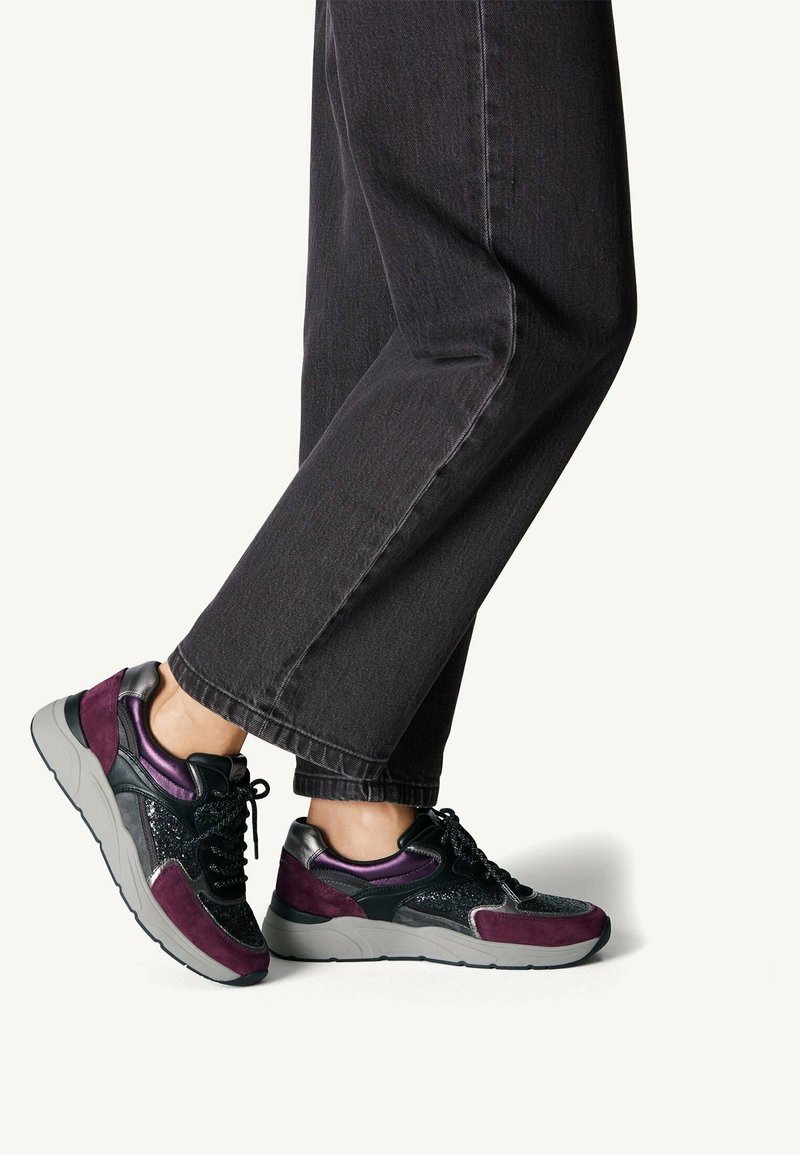 Sneakers con tomaia in rete nera, accenti in suede viola e suola in gomma grigia. Presentano dettagli lucidi neri e viola, superfici testurizzate.