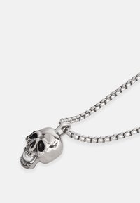 Collana in argento con un pendente a forma di teschio dettagliato con accenti neri e una catena texturizzata. Il pendente evidenzia tratti facciali intricati.