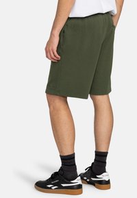 Green cotton blend shorts with an elastic waistband, side pockets, and a straight cut, paired with black sneakers and dark socks.