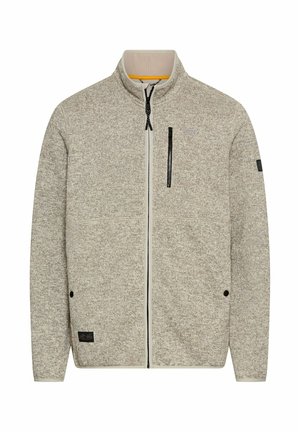 Fleecejakke i lys beige med et tekstureret mønster, fuld frontlynlås, stående krave og en brystlomme med lynlås. Har sorte accenter.