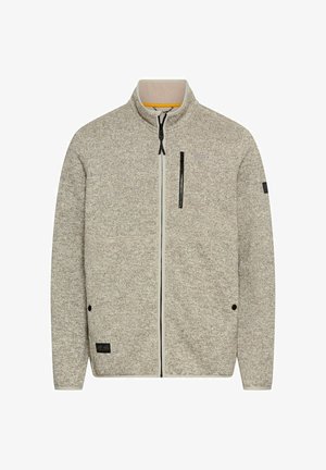 Fleecejakke i lys beige med et tekstureret mønster, fuld frontlynlås, stående krave og en brystlomme med lynlås. Har sorte accenter.