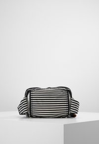 Sac en tissu à rayures noires et blanches avec fermeture éclair, sangle réglable et forme rectangulaire, présentant une surface texturée.
