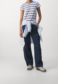 Camiseta de manga corta a rayas en azul claro y marino, combinada con pantalones cargo azul oscuro y una camisa azul clara atada a la cintura.