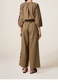 Khaki twee-delige outfit met een tailleriem en opgeblazen mouwen. De top heeft geplooide details en zwarte bloem borduurwerk op de mouwen.