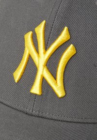 Grå baseballkasket med en broderet gul "NY" logo. Stoffet har en tekstureret finish med synlige syninger.
