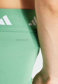 Gröna sportleggings med slät yta, utrustade med en bred midjerem märkt "AEROREADY" och vita detaljremsor.