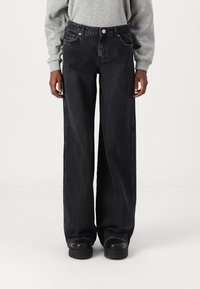 Svarta vida jeans i denim. Har fem fickor, en knappstängning och synlig sömnad. Kombineras med svarta platåskor.