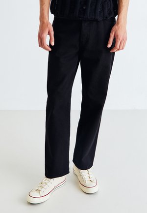 Sorte lige ben bukser lavet af denim, med et klassisk design og en holdbar tekstur. Båret sammen med hvide sneakers med røde detaljer.