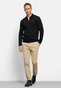 Zwarte langemouwen pullover met een ritsnek, gecombineerd met beige broeken en zwarte schoenen. Gladde stof, casual pasvorm, minimalistisch ontwerp.