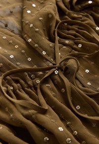 Brunt stof med teksturerede prikker og små reflekterende cirkulære palietter, samlet og bundet med en matchende stofsnor.