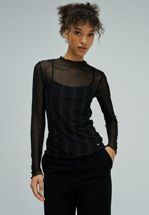 Top negro de manga larga con tela transparente y rayas plateadas verticales, diseño entallado y detalle fruncido en la cintura.