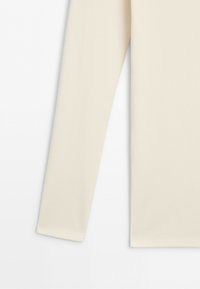 Long cream-colored ribbed fabric sleeve, part of a garment, shown against a white background.