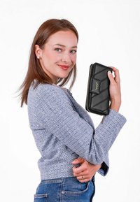 Černá kožená peněženka s prošívaným designem, zipovým uzávěrem a zlatými kovovými doplňky, držena proti bílému pozadí. Jaket z textilního vzoru.