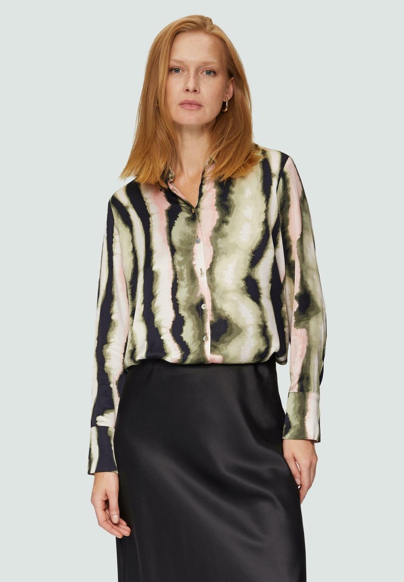 Lange mouw blouse in een groen, zwart en roze abstract patroon. Zachte stof met een kraag en knoopsluiting aan de voorkant. Gecombineerd met een zwarte rok.