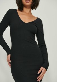 Robe noire à manches longues et décolleté en V, en tissu côtelé, à silhouette ajustée, avec une apparence texturée et une finition lisse.