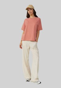 Różowy krótki t-shirt, krótkie rękawy, miękki bawełniany materiał; w połączeniu z kremowymi spodniami cargo i szarymi trampkami; beżowa czapka z akcentem tekstowym.