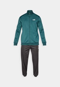 Tirkīza krāsas Puma sporta jaka ar rāvējslēdzēju un logo uz krūtīm, kopā ar melnām Puma sporta biksēm pret vienkāršu balto fona.