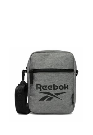 Mała szara torba na ramię marki Reebok z przednią kieszenią na zamek błyskawiczny, regulowanym czarnym paskiem i czarnym logo Reebok z przodu.