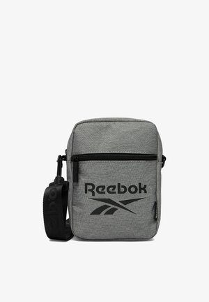Mała szara torba na ramię marki Reebok z przednią kieszenią na zamek błyskawiczny, regulowanym czarnym paskiem i czarnym logo Reebok z przodu.
