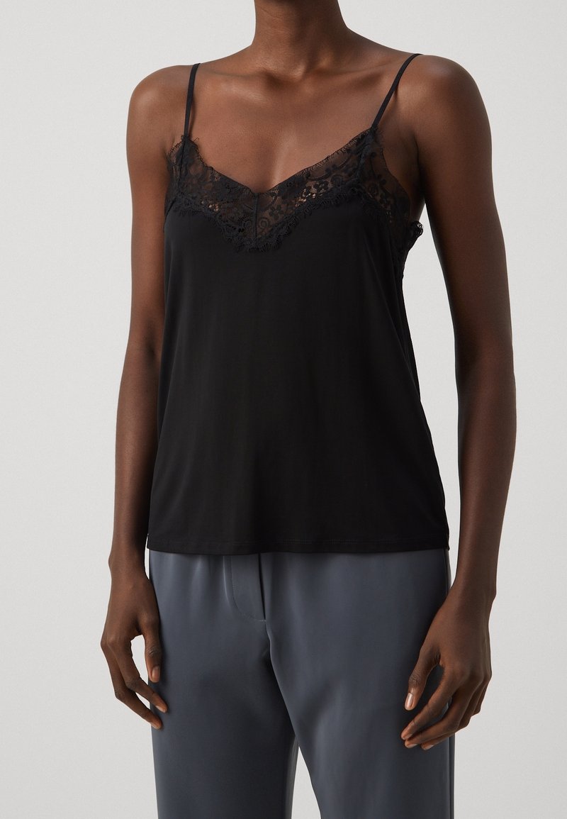 Débardeur noir avec bordure en dentelle, fines bretelles ajustables, tissu lisse et encolure en V. Associé à un pantalon gris ample.