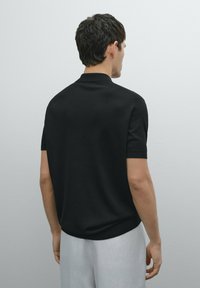 Polo shirt nero a maniche corte in maglia con colletto e polsini a costina, caratterizzato da una trama liscia e un orlo dritto.