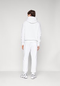 Sweatshirt blanc avec capuche, pantalon de jogging blanc assorti et baskets blanches. Tissu doux, coupe décontractée, coutures visibles et poignets côtelés.
