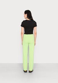 Top preto de mangas curtas com bordas rendadas, combinado com calças verde claro de cintura alta e caneladas. As calças apresentam punhos elásticos.