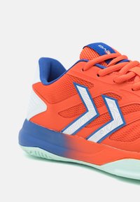 Jasnopomarańczowy but sportowy z niebieskimi akcentami, siateczkową cholewką, białymi teksturowanymi paskami oraz gumową podeszwą z gradientem od niebieskiego do miętowego.