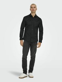 Zwarte blouse met lange mouwen en een gekraagde hals, vooraan met knopen, gecombineerd met donkere jeans en witte sneakers met een beige zool.