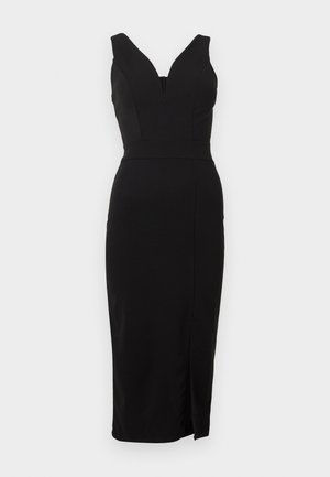 Melna, bezroku pieguloša vidēja garuma kleita ar dziļu V veida izgriezumu un sānu šķēlumu uz gaiši pelēka fona.