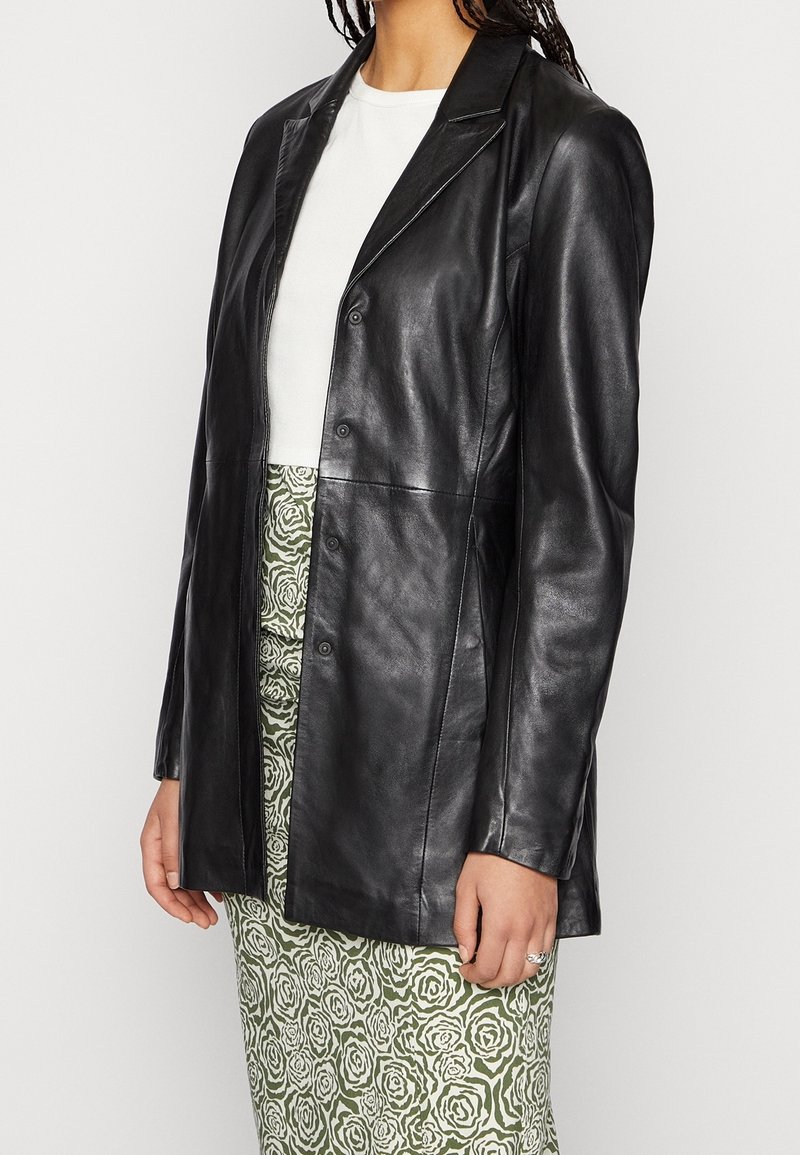 Person wearing a black leather buttoned jacket over a white top with a green and white floral patterned skirt.