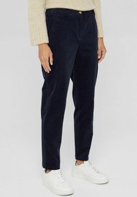 Marineblaue Cordhosen mit einer lockeren Passform, ausgestattet mit einem Knopfverschluss und seitlichen Taschen, kombiniert mit weißen Sneakers. Weiche Textur, gerades Bein Design.