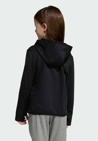 Čierna mikina s kapucňou a textúrovanou látkou, s voľným strihom a mäkkým interiérom, kombinovaná so svetlošedými teplákmi.