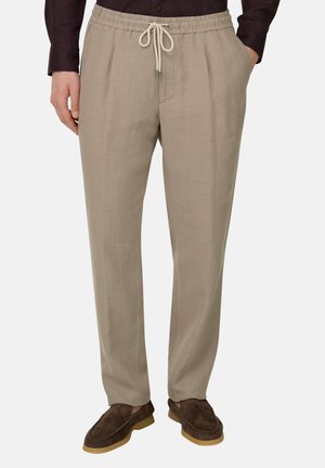 Beige Leinenhose mit Kordelzug, getragen mit dunklem Langarmshirt und braunen Wildleder-Slippern mit Gummisohlen.