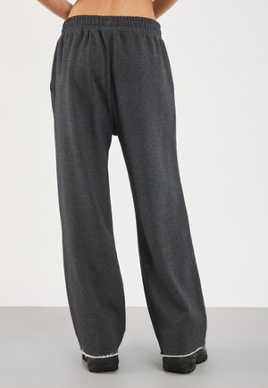 Pantalones de chándal sueltos de color gris oscuro con cintura elástica y dobladillos sin rematar, usados con zapatos negros, vistos desde atrás sobre un fondo liso.