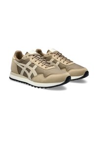 Beige athletic shoes with suede and mesh upper, featuring cream accents and laces, black rubber sole, and classic running shoe design.