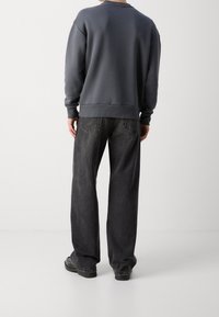 Sweatshirt gris à col rond et ourlet en côtes, associé à un jean foncé, ample, avec poches arrière et coutures discrètes.