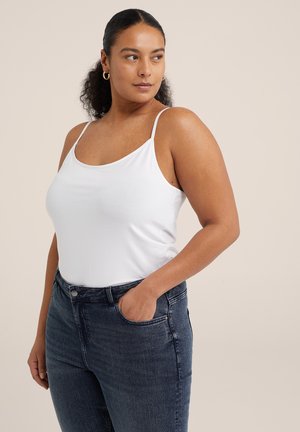 Witte mouwloze top met dunne bandjes, gemaakt van een zachte stof. Gecombineerd met donkerblauwe high-waisted jeans met voorzakken en een getailleerd ontwerp.