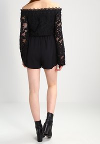 Romper negro sin mangas con encaje de manga larga, cintura elástica y pantalones cortos. Combinado con botines de tacón negros. Textura de tela suave.