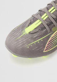 Sivé futbalové kopačky s textúrovaným zvrškom, s neonovo žltými a ružovými akcentmi, okrúhle špičky a tvarované kolíky pre lepšiu trakciu. Viditeľné logo "ULTRA".