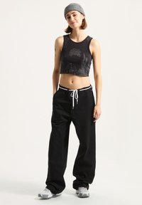 Black cropped tank top with a graphic design and gray accents, paired with loose black pants featuring a contrast drawstring and sneakers.