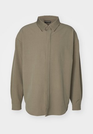 Chemise à manches longues surdimensionnée en vert olive, avec un col pointu, des manches longues et un ourlet droit avec une finition légèrement texturée.