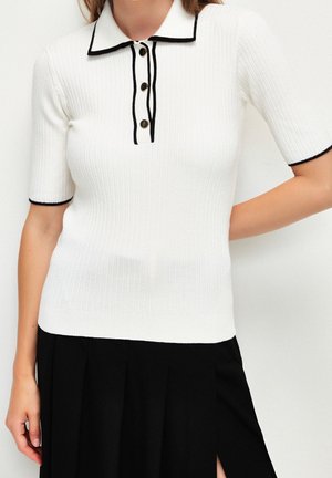 White ribbed short-sleeve polo shirt with black trim on collar and sleeves, button placket, paired with a black pleated skirt.
