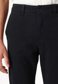 Pantalones de algodón negros con un corte recto, que cuentan con un cierre de botón, bolsillos delanteros y traseros, y una textura sutil.