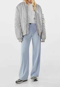 Silver bomber jacket with ribbed cuffs, white cropped sweatshirt, light blue wide-leg trousers, and gray sneakers with white accents.