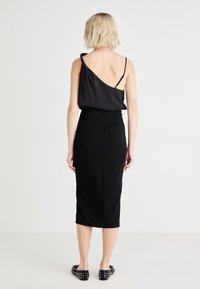 Svart klänning med en axel design och kroppsnära silhuett. Slät tyg, knälång, med en rak fåll längst ner.