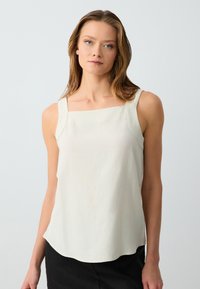 Top senza maniche di un beige chiaro con scollatura quadrata e spalline larghe, realizzato in un tessuto liscio, con una texture sottile e un orlo curvo.