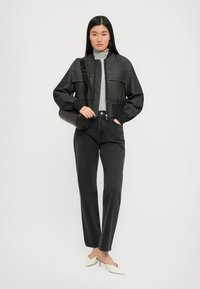 Veste bomber en tricot gris avec poches avant, associée à un col roulé gris clair et un jean noir taille haute. Mules à talons blancs.